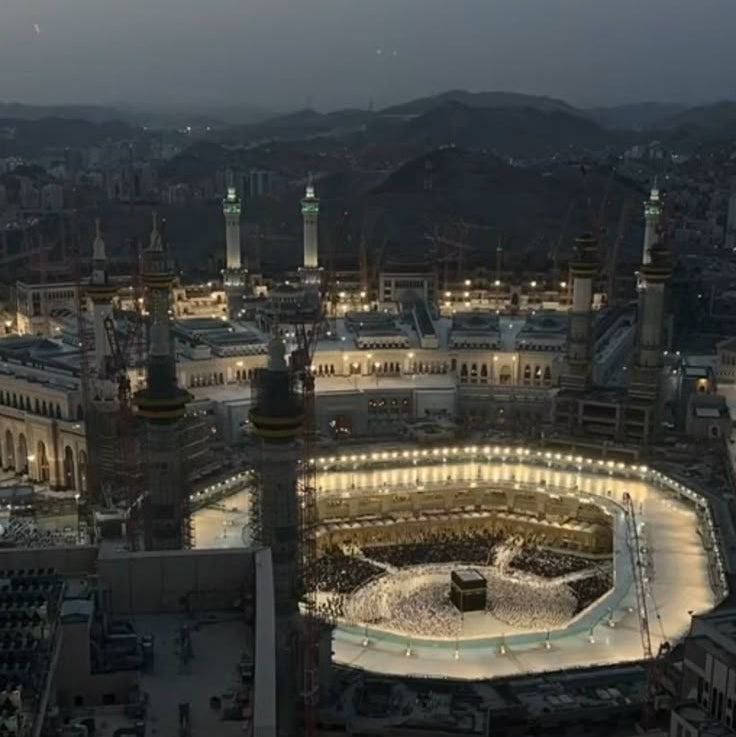 Aerial view of a illuminated mosque complex with mountains in the background