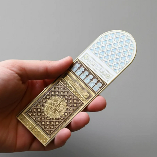 Hand holding a small, ornate book with intricate designs on a gray background