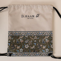 An off-white drawstring bag with a decorative border and black drawstrings, featuring the brand name 'ILHAAM' printed on the front, set against a plain beige background.