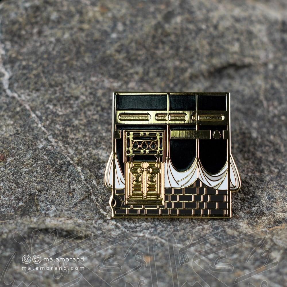 Gold and black stainless steel pin inspired by the door of the Kaaba with detailed Islamic architectural design
